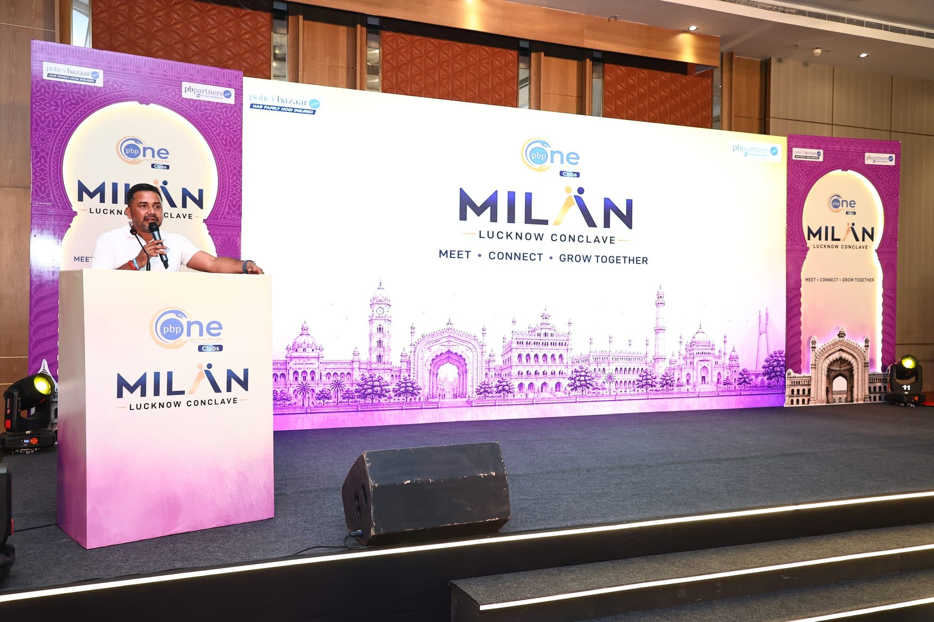 PolicyBazaar MILAN Conclave speaker at podium with Lucknow skyline stage backdrop